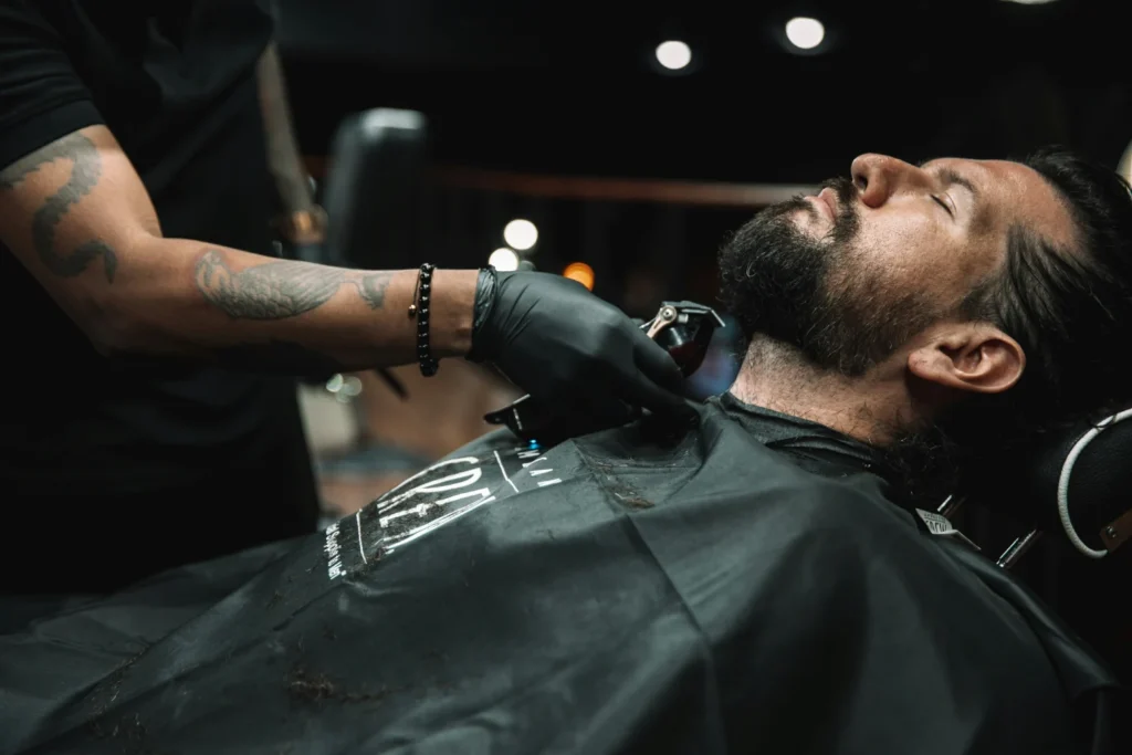 Barber w czarnych rękawiczkach trzyma maszynkę przy brodzie klienta
